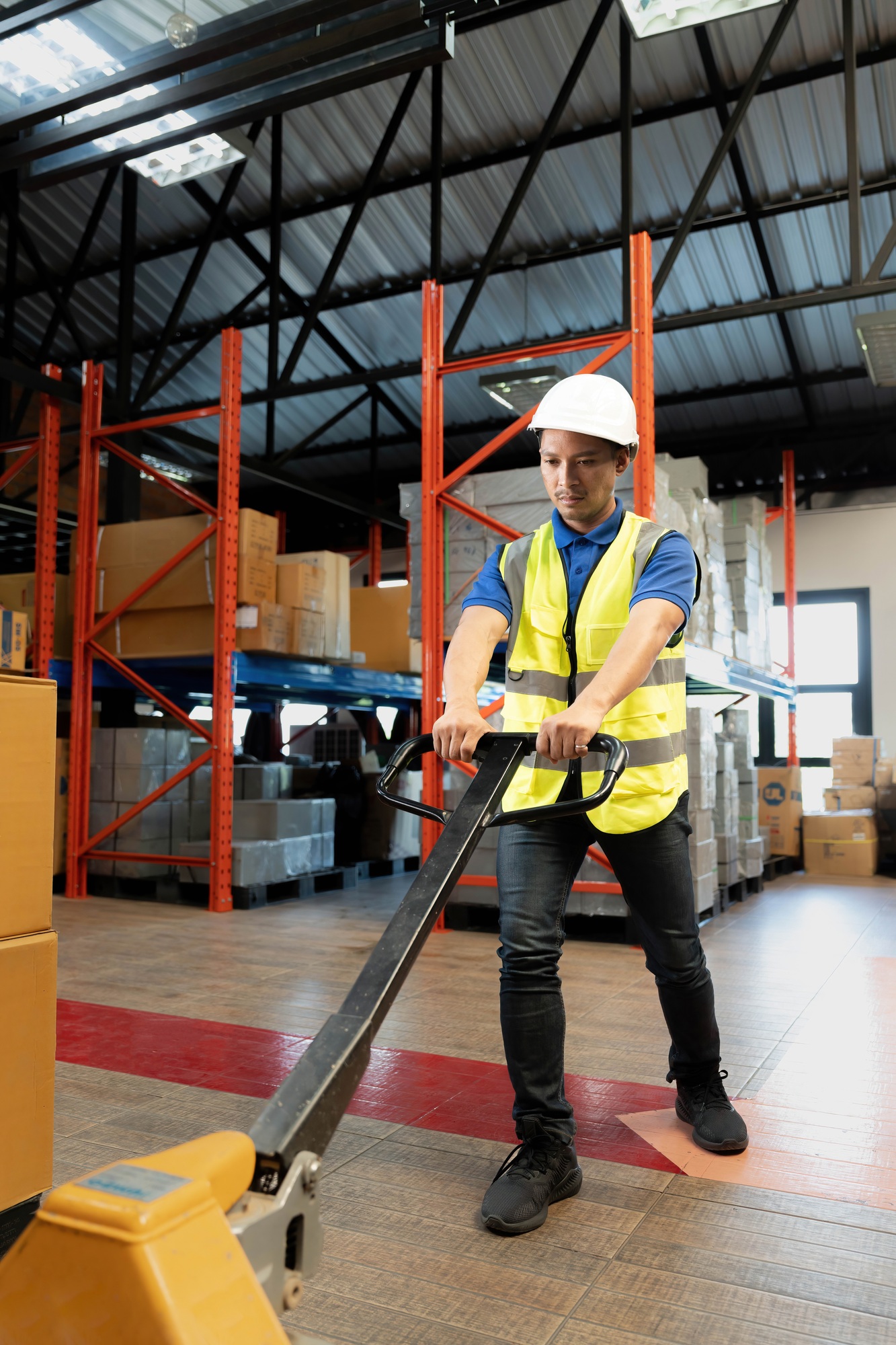 Portrait, Tired millennial Asian male warehouse worker pulling a pallet truck, suffering from back