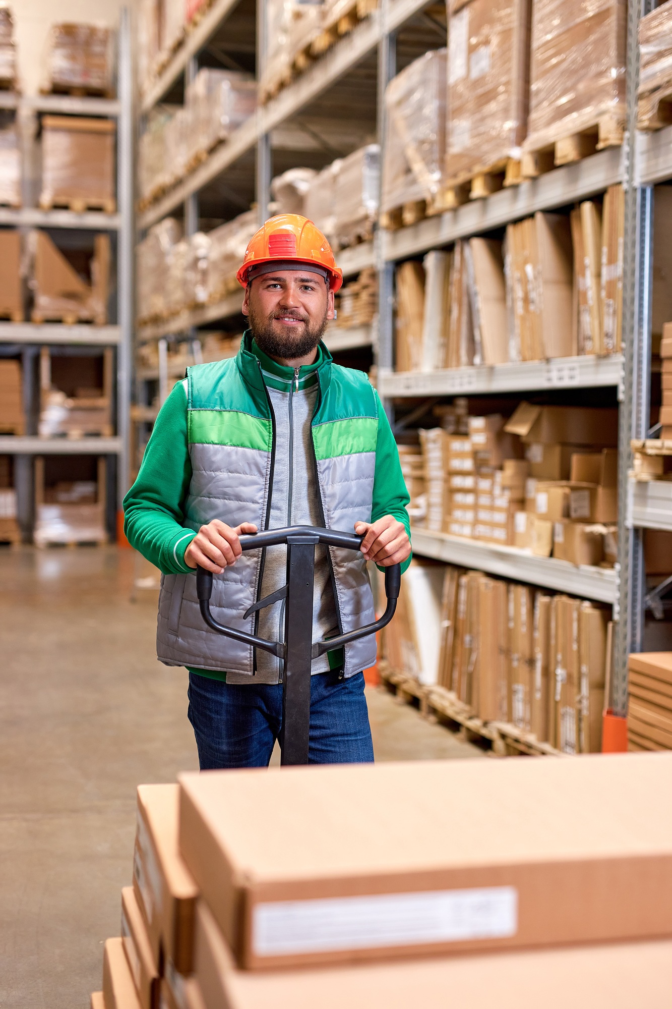 warehouse worker with manual pallet jack, working in storage room, transporting cardboard boxes